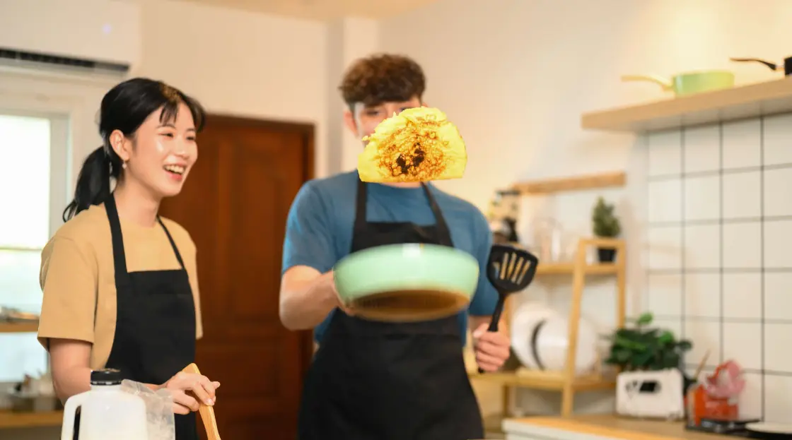 Playful couple flipping pancake and sharing laughter in kitchen